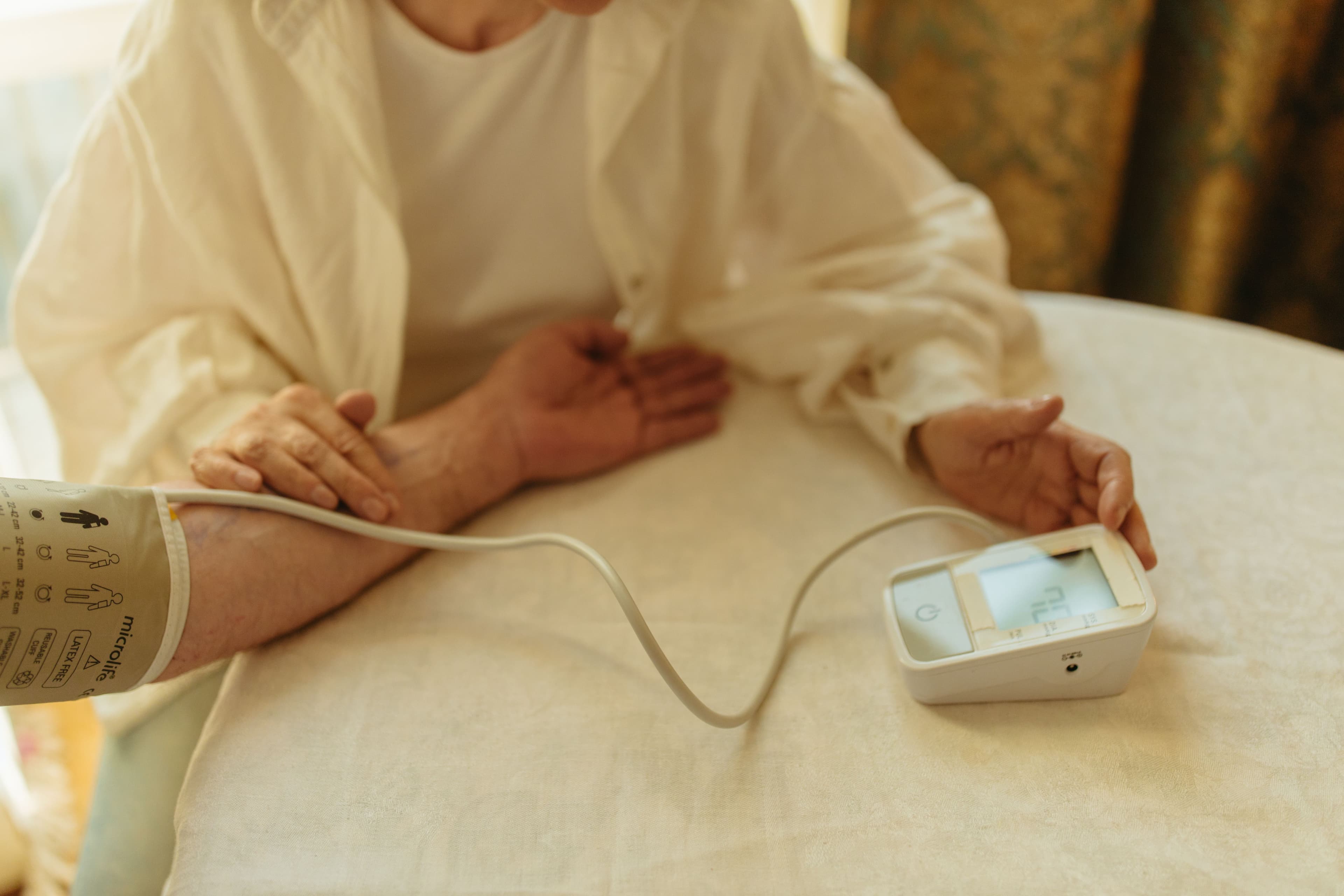 Older woman checking her blood pressure at home with a monitor and arm cuff on the table.