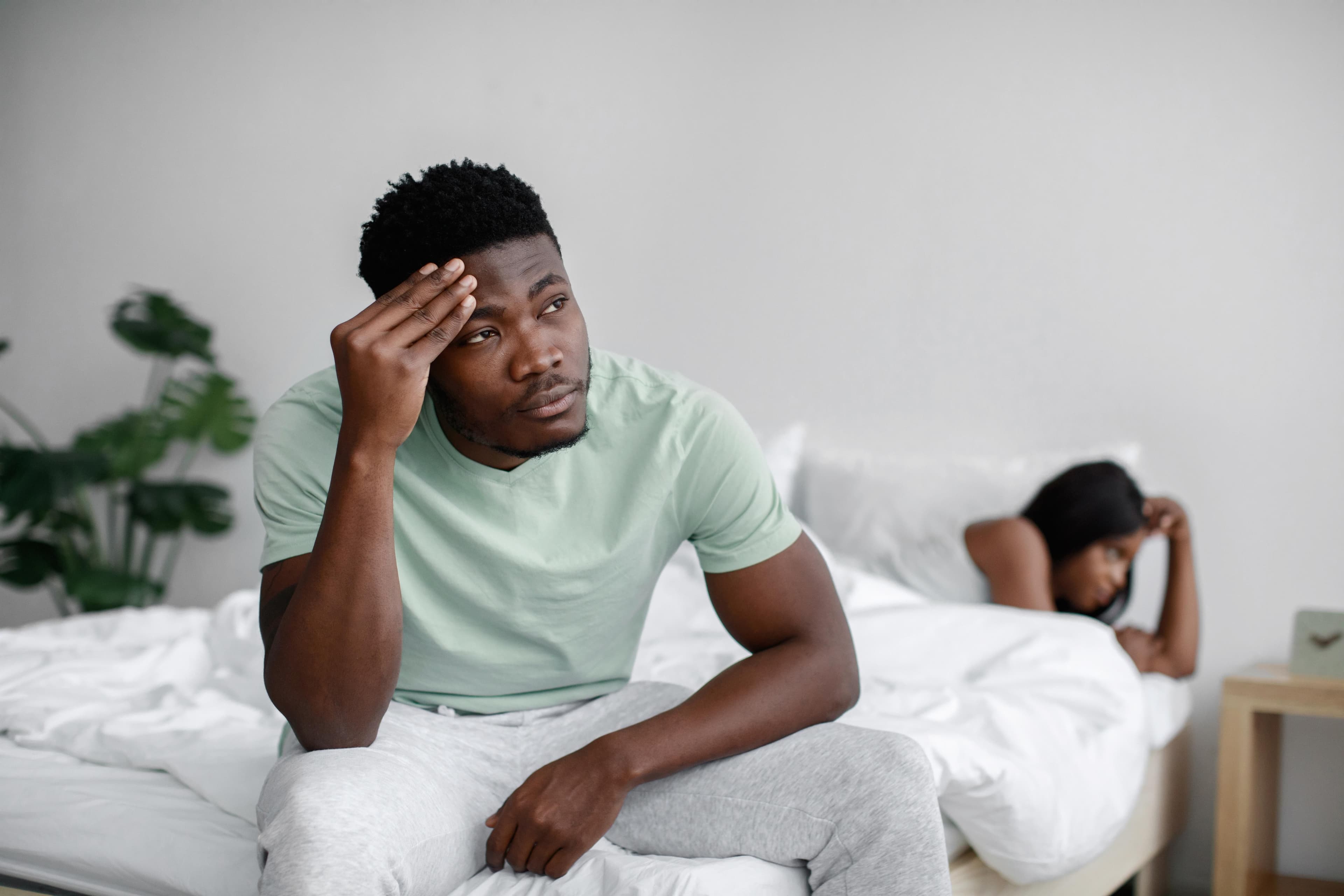 Man sitting on the edge of the bed with his partner turned away, showing the strain erectile dysfunction can cause.