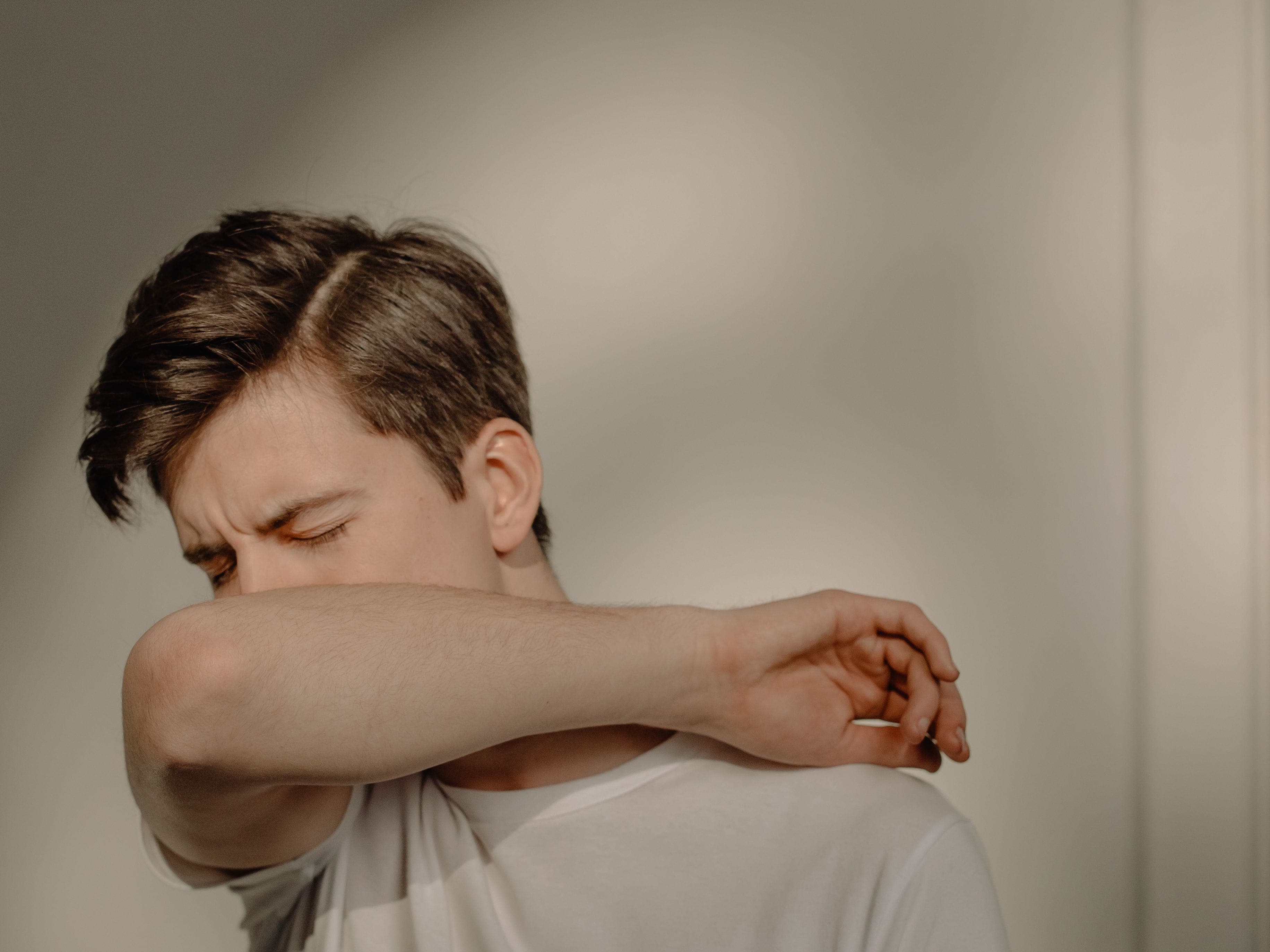 Young man coughing into his elbow, one of the asthma symptoms a preventer inhaler like Fostair helps control.