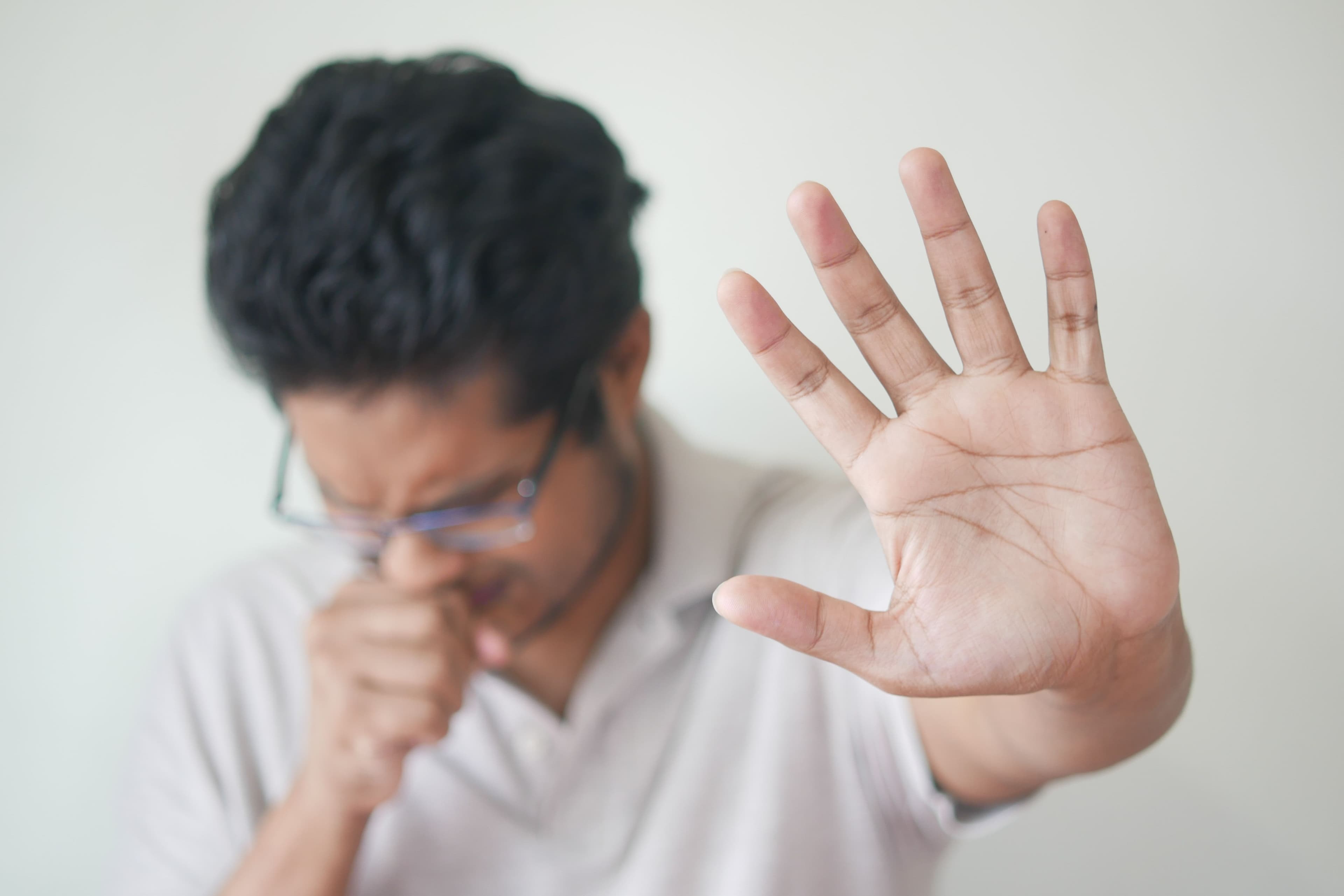 A man coughing into his hand, palm raised, the kind of symptom that leads people to reach for an inhaler